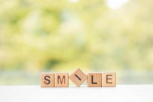 La palabra sonrisa está escrita en cubos de madera sobre un fondo verde de verano Primer plano de elementos de madera