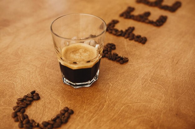 Palabra de texto de café hecha de aromáticos granos de café tostados y una taza de café expreso caliente en la mesa