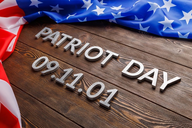 Las palabras día del patriota colocadas con letras de metal plateado en la superficie de una tabla de madera con una bandera de estados unidos arrugada