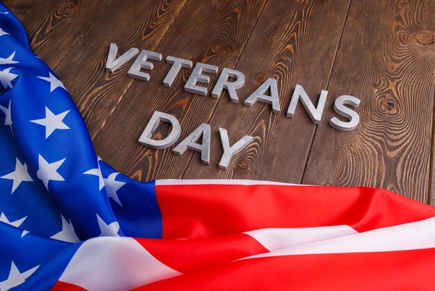 Las palabras día de los veteranos colocadas con letras de metal plateado en la superficie de una tabla de madera con una bandera de estados unidos arrugada