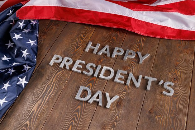 Palabras feliz día de los presidentes colocadas con letras reales en una tabla de madera cerca de la bandera estadounidense