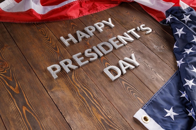 Palabras feliz día de los presidentes colocadas con letras reales en una tabla de madera cerca de la bandera estadounidense