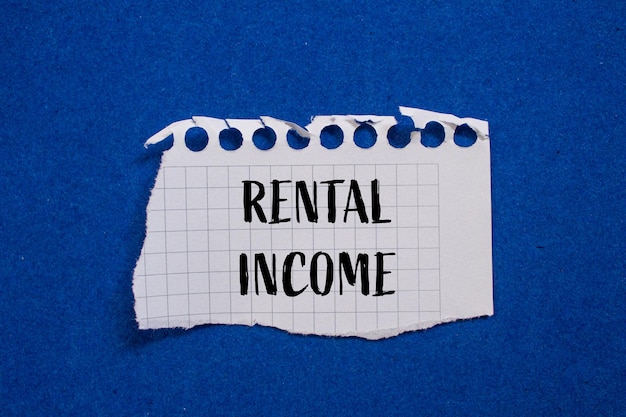 Foto palabras de ingresos de alquiler escritas en papel blanco rasgado con fondo azul símbolo conceptual de ingresos de arrendamiento espacio de copia