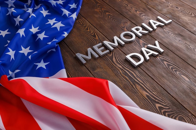 Las palabras memorial day colocadas con letras de metal plateado en la superficie de una tabla de madera con una bandera de estados unidos arrugada