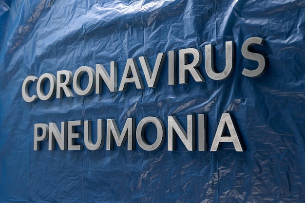 Las palabras neumonía por coronavirus colocadas con letras plateadas en una película de plástico azul arrugada en composición en perspectiva