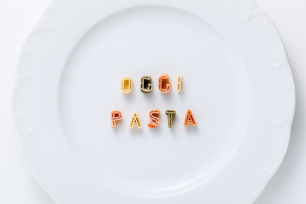 Palabras OGGI PASTA de pasta seca multicolor en un plato blanco.