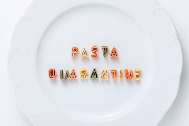 Palabras PASTA CUARENTENA de pasta seca multicolor en un plato blanco.