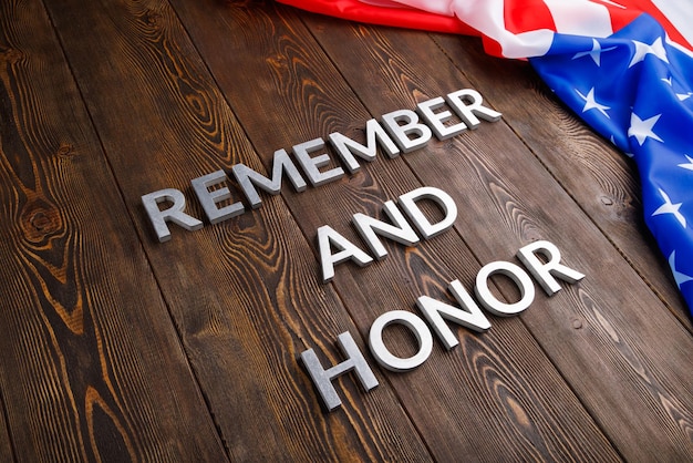 Las palabras recuerdan y honran colocadas con letras de metal plateado sobre fondo de madera con la bandera de EE.UU. en el lado derecho