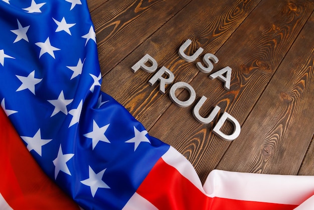 Palabras USA orgullosas puestas con letras de metal plateado en una superficie de madera marrón con bandera de los Estados Unidos de América