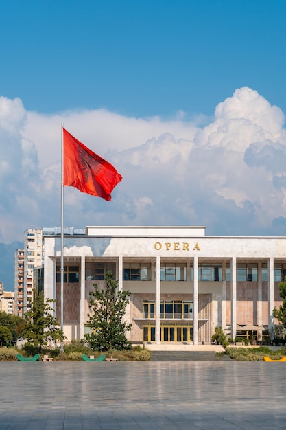 Palacio de la Cultura u Ópera en la Plaza Skanderbeg en Tirana y la bandera de Albania moviéndose en el viento