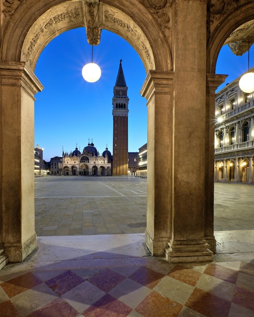 Palacio Ducal de Venecia, torre Campanile en la Piazza di San Marco visible a través del arco antiguo con lámpara de calle circular. Velada romántica, noche en Venecia, Italia.