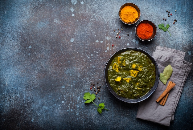 Palak paneer, plato indio vegetariano tradicional con paneer de queso, puré de espinacas y especias. Paneer verde indio en cuenco de cerámica rústica sobre fondo de hormigón, vista superior y espacio para texto