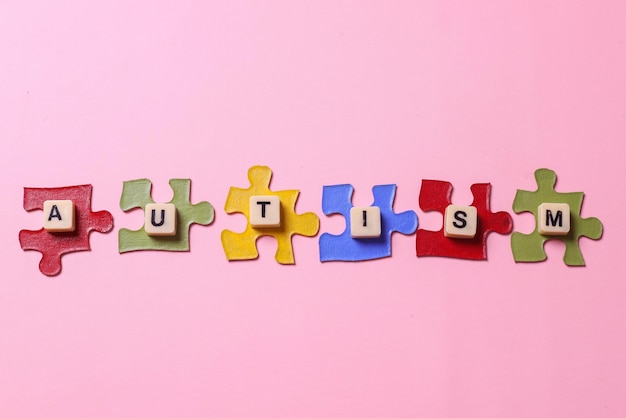 palavra autismo em peças coloridas de quebra-cabeças em um fundo rosa Dia de conscientização do autismo