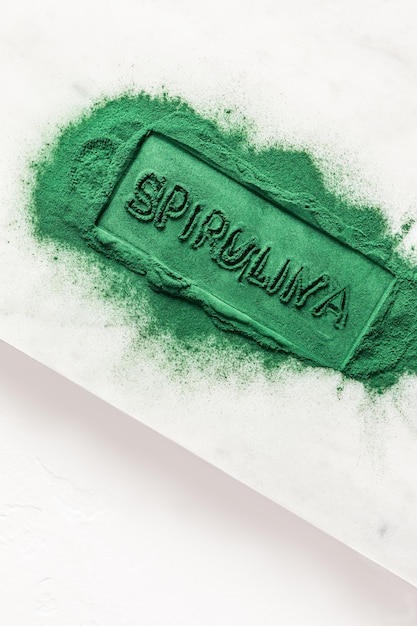 Palavra de espirulina destacada em pó de algas orgânicas verdes espalhadas Vista vertical com fundo branco Apresentação do produto