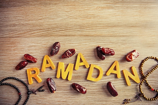 Foto palavra de ramadã com letras de madeira rosário e tâmaras secas na mesa