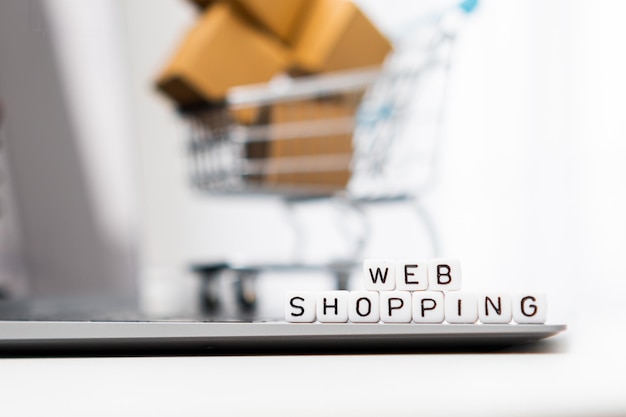 Palavras de compras na Web em cubos colocados no laptop e um carrinho de compras de brinquedo com caixas de papelão