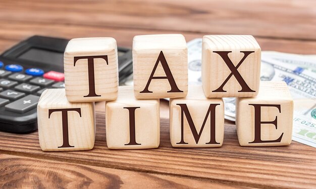 Palavras TAX TIME em cubos de madeira e calculadora com dinheiro na mesa Conceito de negócio