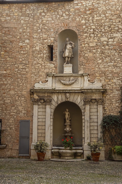 Palazzo Martinengo Cesaresco Novarino-Palast. Innenhof mit kleinem Brunnen mit schönen Statuen und Steindekor in schäbiger Wand. Alte Skulptur mit kleinem Brunnen und Pflanzen und Blumen in Töpfen.