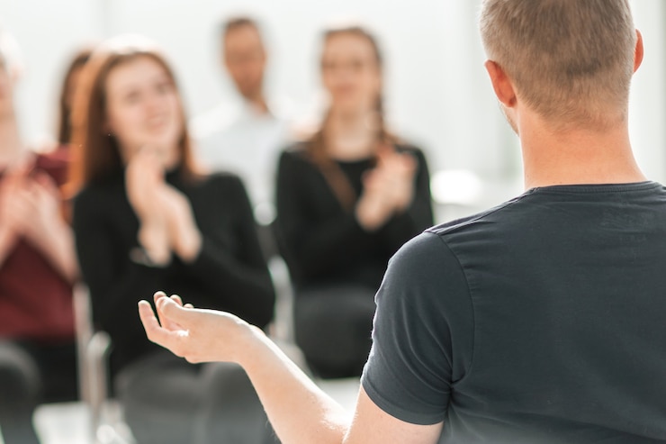 Foto palestrante e um grupo de jovens sentados em uma sala de conferências