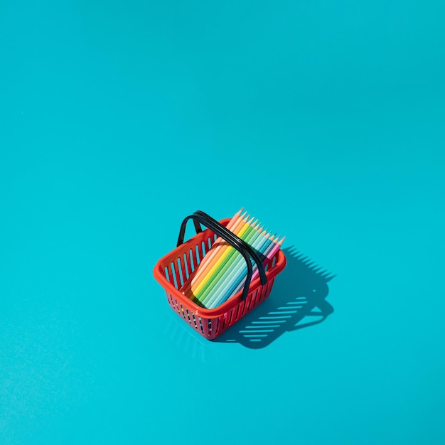 Paleta de arco iris para colorear crayones en cesta de compras roja sobre fondo azul Concepto mínimo