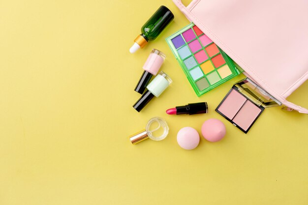 Paleta de sombras de verão brilhante e produtos de maquiagem em bolsa cosmética rosa sobre fundo verde