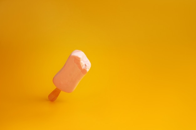 paleta de helado rosa en la pared amarilla mordida un pedazo