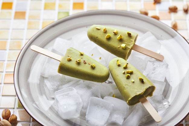 Paleta de pistacho casera congelada en un tazón de hielo en la mesa de mosaico refrescante paleta de jugo verde congelado en la vista superior del palillo copia espacio