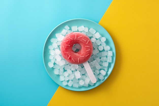 Paleta de rosquilla de fresa y hielo picado en el cuadro amarillo y azul