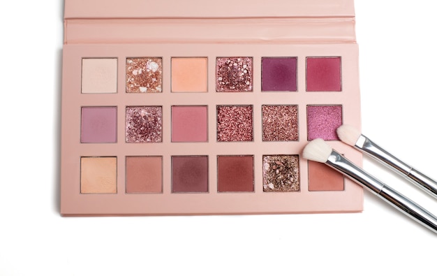 Paleta de sombras de ojos de colores rosados con dos pinceles cosméticos sobre un fondo blanco.