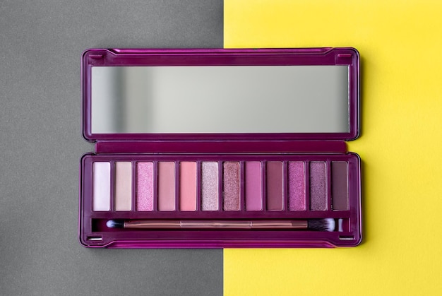 Paleta de sombras de ojos profesional abierta en colores rosas en la última tendencia de fondo de papel iluminador gris y amarillo Paleta con espejo y pincel para maquillaje de ojos de día y de noche