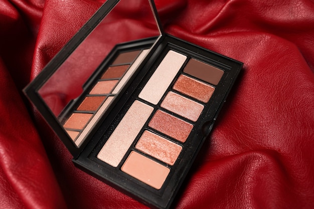 Foto paleta de sombras de ojos en tonos marrones, sombras de ojos mate y brillantes sobre fondo de cuero rojo, vista superior. paleta de sombras de ojos de otoño