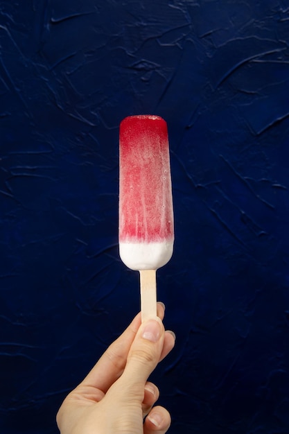 Paletas con arándanos rojos en la mano Fondo azul oscuro