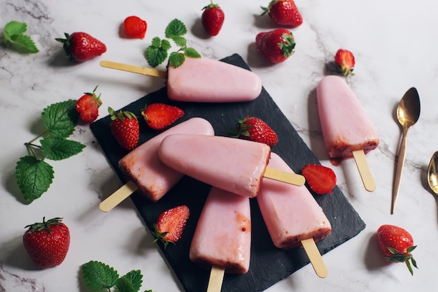 Paletas caseras de resma de hielo de fresa con yogur helado y hojas de menta en pizarra negra y mesa de mármol de enfoque suave