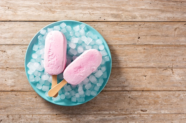 Paletas de fresa y hielo picado en placa azul sobre mesa de madera