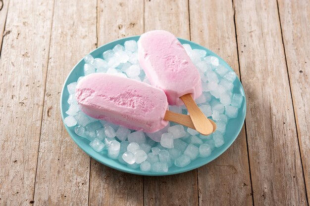 Paletas de fresa y hielo picado en placa azul sobre mesa de madera