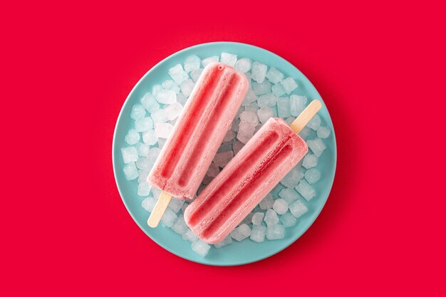 Paletas de fresa con hielo sobre superficie roja