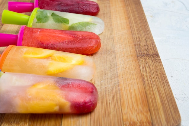 Paletas frutales coloridas caseras en una tabla de madera y contra.