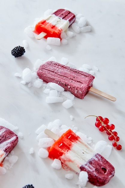 Paletas heladas caseras de bayas tricolores con hielo y bayas sobre fondo de mármol. Copie el espacio para el texto.