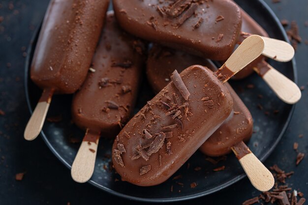 Paletas de helado de chocolate negro con chocolate rallado en un plato oscuro. De cerca