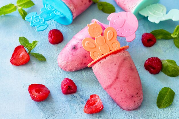 Paletas de helado para niños sorbete de fresa y frambuesa sobre fondo de hormigón azul