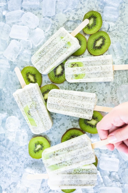 Paletas de kiwi, coco y chía con kiwi fresco y hielo en bandeja de metal.