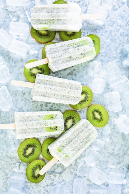 Paletas de kiwi, coco y chía con kiwi fresco y hielo en bandeja de metal.