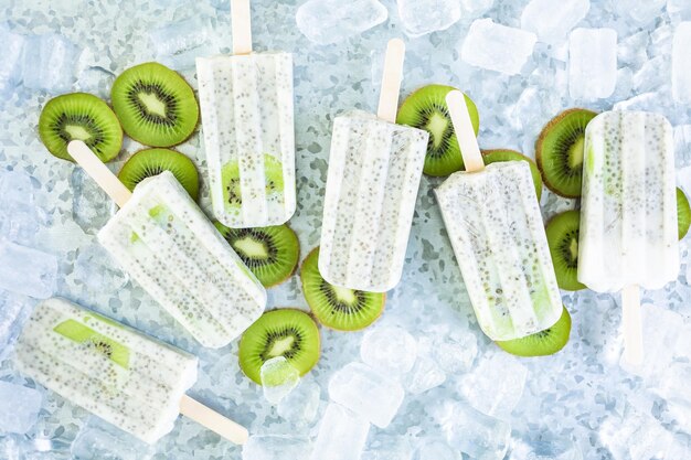 Paletas de kiwi, coco y chía con kiwi fresco y hielo en bandeja de metal.