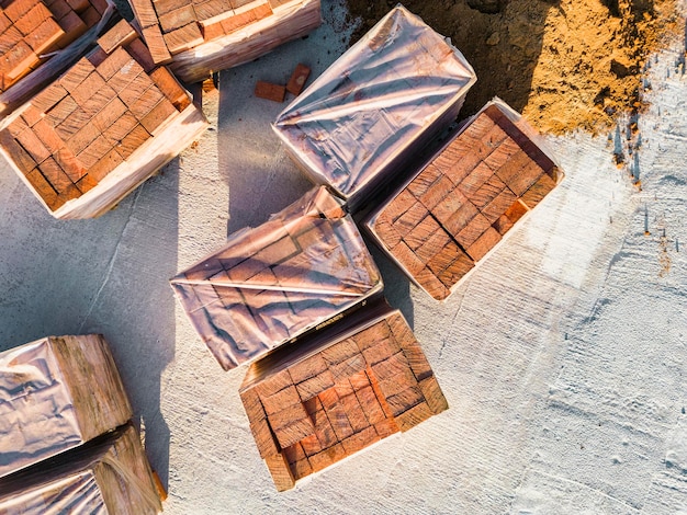 Paletas con ladrillos cerámicos rojos en el techo de un edificio en construcción Trabajos preparatorios para la colocación de ladrillos Vista superior del sitio de construcción