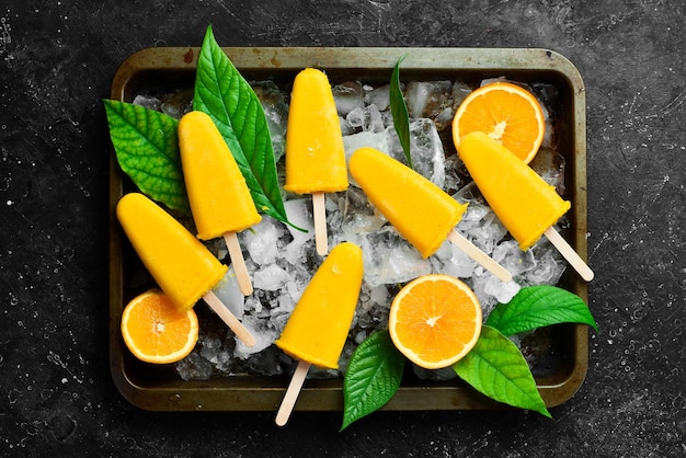 Paletas de naranja congeladas en una bandeja Dulces fríos de verano Sobre un fondo de piedra negra Vista superior