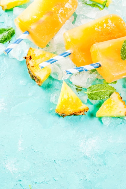 Paletas de piña caseras sobre hielo con rodajas de piña fresca y menta sobre fondo azul claro