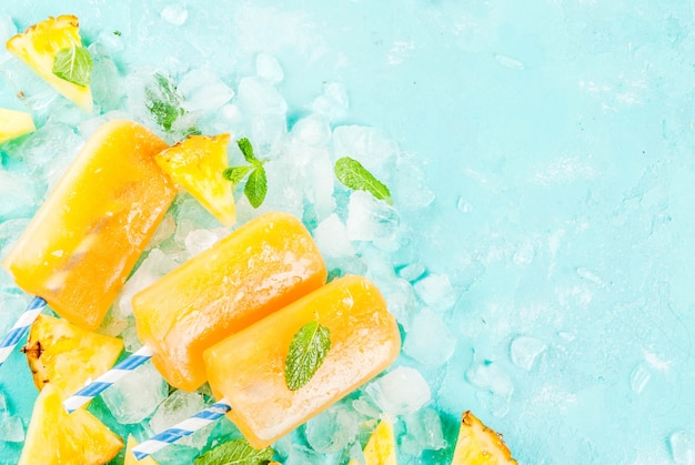 Paletas de piña caseras sobre hielo con rodajas de piña fresca y menta sobre fondo azul claro