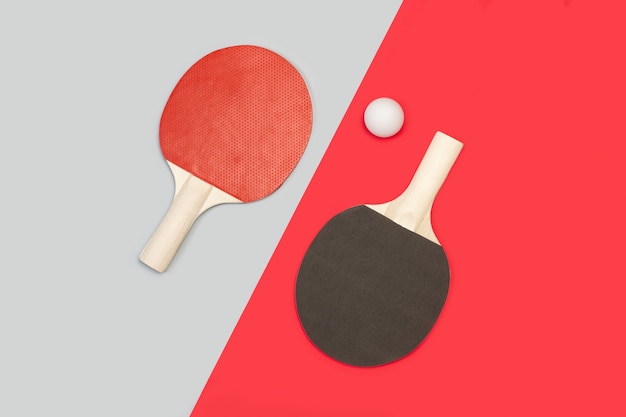 Paletas de ping pong rojas y negras con una bola blanca sobre una gris y roja