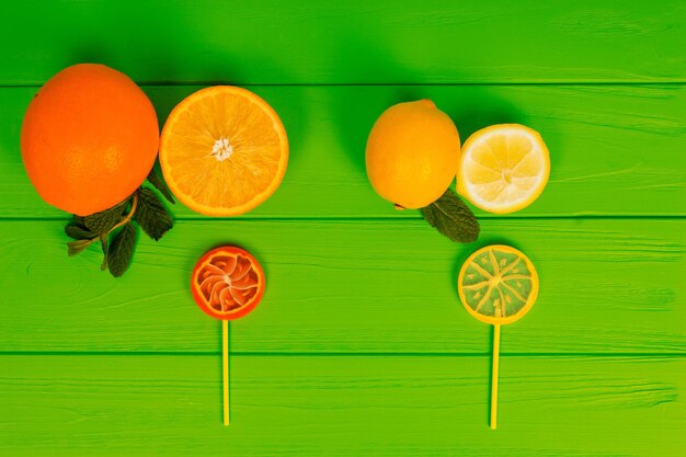 Paletas sabrosas como una naranja y un limón en la placa verde de madera cerca de deliciosas rodajas de pera y naranja con una ramita de menta