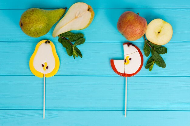 Foto paletas sabrosas como una pera y una manzana sobre una placa de madera turquesa cerca de deliciosas rodajas de pera y manzana con una ramita de menta